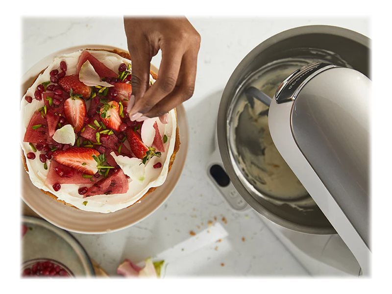 Kenwood Titanium Chef Baker XL i bakgrunden medan en tårta dekoreras med jordgubbar och granatäpple i förgrunden.